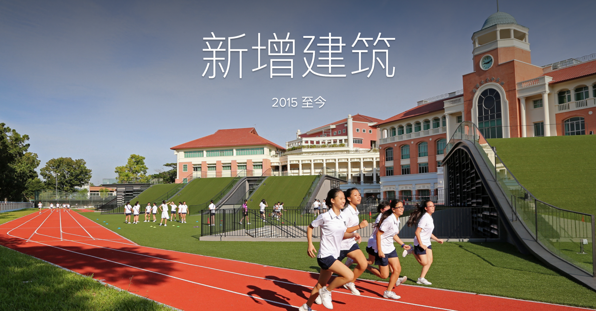 Students run on a red track beside a green field, with a large school building and clock tower behind.